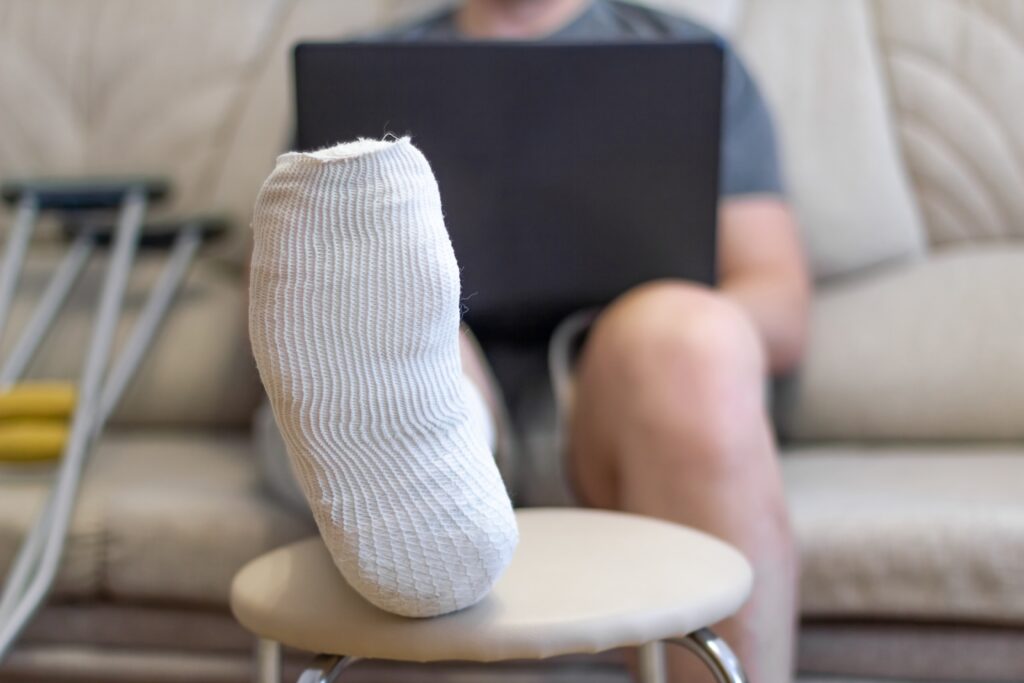 Man elevates his broken foot on a stool while he looks up legal options for defective product claims.